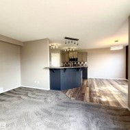 Open-concept living area with gray carpeting, wood-finish flooring, and a kitchen island with seating - 