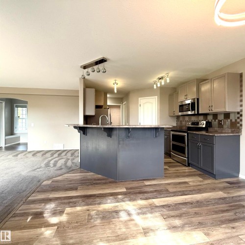 Kitchen featuring wood-finish flooring, two-tone cabinetry, stainless steel appliances, a tiled backsplash, and an island with counter seating - 910 Oakland Boulevard, Devon, AB 