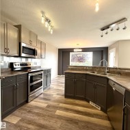 Two-tone cabinetry with stainless steel appliances, wood-finish flooring, undermount double basin sink, and track lighting - 