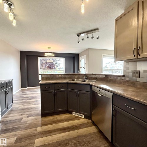 L-shaped kitchen with stainless steel sink, integrated dishwasher, dark wood-finish cabinetry, and wood-finish flooring - 910 Oakland Boulevard, Devon, AB 