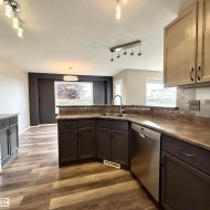L-shaped kitchen with stainless steel sink, integrated dishwasher, dark wood-finish cabinetry, and wood-finish flooring - 