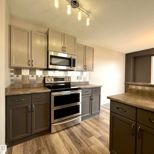 Stainless steel double oven range, stainless steel microwave, track lighting, wood-finish flooring, and two-tone cabinetry - 910 Oakland Boulevard, Devon, AB 
