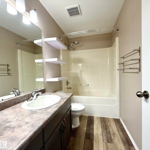 Bathroom featuring a single vanity with an integrated sink, a rectangular mirror, wood-finish flooring, and a bathtub with shower - 910 Oakland Boulevard, Devon, AB 