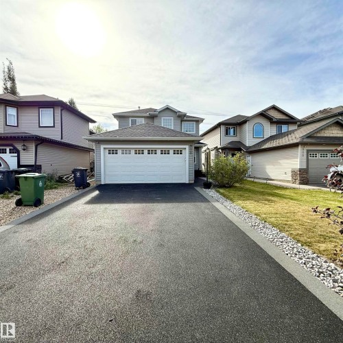 Two-story home featuring a two-car garage with overhead lighting, a shingle roof, and a paved driveway with a gravel border - 910 Oakland Boulevard, Devon, AB 