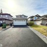 Two-story home featuring a two-car garage with overhead lighting, a shingle roof, and a paved driveway with a gravel border - 910 Oakland Boulevard, Devon, AB 