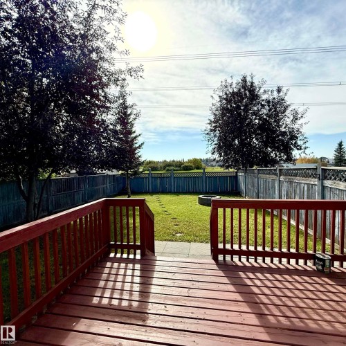 Expansive backyard featuring a wood deck, manicured lawn, and mature trees, surrounded by a privacy fence - 910 Oakland Boulevard, Devon, AB 