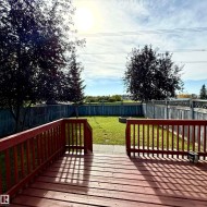 Expansive backyard featuring a wood deck, manicured lawn, and mature trees, surrounded by a privacy fence - 