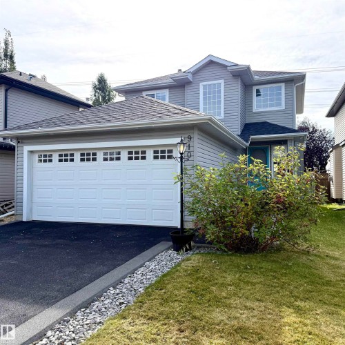 Two-story exterior with light gray siding, an attached garage featuring multiple window inserts, and an asphalt driveway - 910 Oakland Boulevard, Devon, AB 