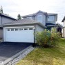 Two-story exterior with light gray siding, an attached garage featuring multiple window inserts, and an asphalt driveway - 910 Oakland Boulevard, Devon, AB 