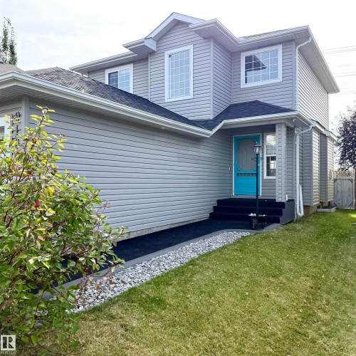 Two-story residence featuring light gray siding, white window trim, a prominent front entrance with a turquoise screen door, dark steps, and a paved walkway bordered by decorative stone - 910 Oakland Boulevard, Devon, AB 