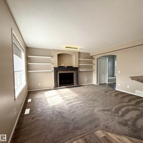 Living area featuring a fireplace with a dark wood mantel and surround, built-in shelving, and carpeting - 910 Oakland Boulevard, Devon, AB 