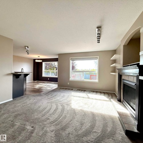 Living area featuring a fireplace with tile surround, built-in shelving, and large windows - 910 Oakland Boulevard, Devon, AB 