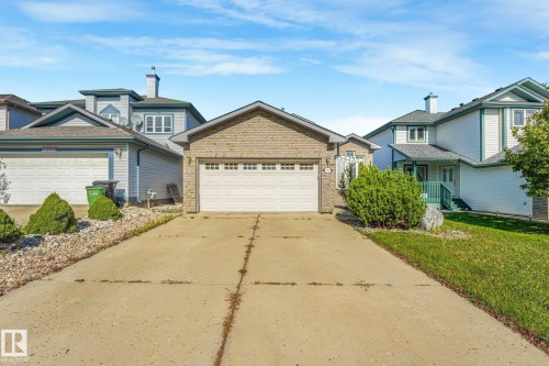 Brick facade with a white garage door, concrete driveway, and front lawn with mature shrubbery - 1271 Ormsby Lane Nw, Edmonton, AB 