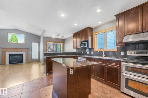 Kitchen featuring wood cabinetry, stainless steel appliances, and a central island with a granite-style countertop - 1271 Ormsby Lane Nw, Edmonton, AB 