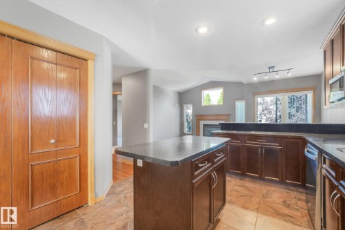 Kitchen featuring dark wood cabinetry, granite-style countertops, integrated dishwasher, and tile flooring - 1271 Ormsby Lane Nw, Edmonton, AB 