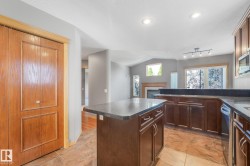 Kitchen featuring dark wood cabinetry, granite-style countertops, integrated dishwasher, and tile flooring - 