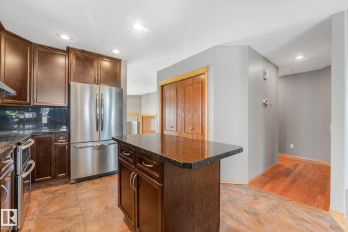 Kitchen featuring rich wood-finish cabinetry, stainless steel appliances, dark stone countertops, and tile flooring - 1271 Ormsby Lane Nw, Edmonton, AB 