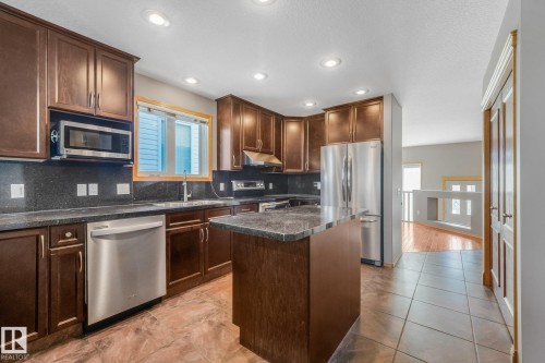 Kitchen featuring dark wood-finish cabinetry, stainless steel appliances, dark stone countertops, and a central island - 1271 Ormsby Lane Nw, Edmonton, AB 