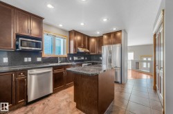 Kitchen featuring dark wood-finish cabinetry, stainless steel appliances, dark stone countertops, and a central island - 