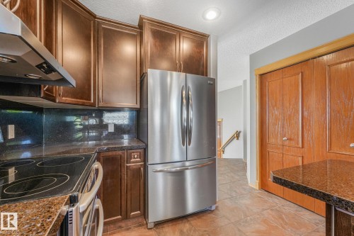 Stainless steel refrigerator, integrated stovetop, dark wood-finish cabinetry, speckled countertops, and tile flooring - 1271 Ormsby Lane Nw, Edmonton, AB 