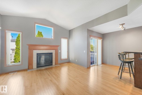 Vaulted ceiling, fireplace with wood mantel and tile surround, wood-finish flooring, sliding glass door, and track lighting fixture - 1271 Ormsby Lane Nw, Edmonton, AB 