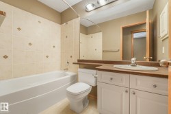 Bathroom featuring a white bathtub, tiled shower surround with accent tiles, vanity with integrated sink, and white cabinetry - 
