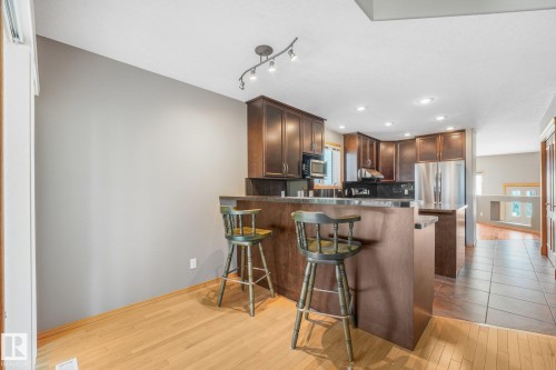 Kitchen featuring dark wood cabinetry, stainless steel refrigerator, dark countertops, and recessed lighting - 1271 Ormsby Lane Nw, Edmonton, AB 