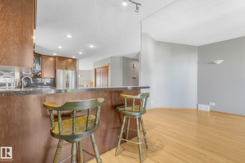 Kitchen bar with a stone-finish countertop, wood-finish cabinetry, stainless steel appliances, and light wood-finish flooring - 1271 Ormsby Lane Nw, Edmonton, AB 