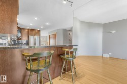 Kitchen bar with a stone-finish countertop, wood-finish cabinetry, stainless steel appliances, and light wood-finish flooring - 