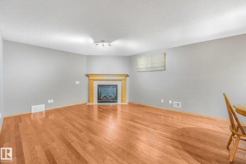 Hardwood-style flooring throughout, featuring a fireplace with a wood mantel, track lighting, and neutral wall tones - 1271 Ormsby Lane Nw, Edmonton, AB 