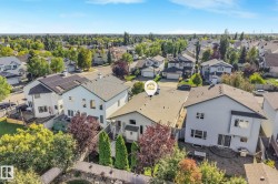 Property featuring a shingled roof, attached deck, mature landscaping, and a paved patio area - 