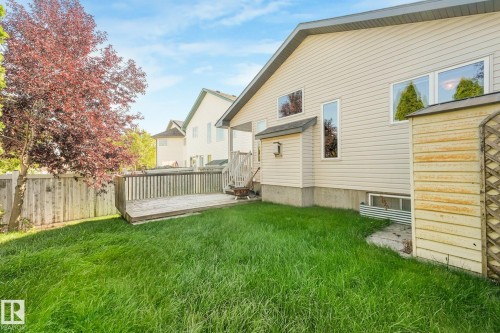 Spacious backyard with a wooden deck, privacy fence, mature tree, and light-colored siding - 1271 Ormsby Lane Nw, Edmonton, AB 