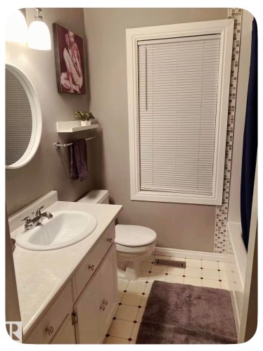 White vanity with an integrated sink, round mirror, and tile flooring - 10649 125 Street Nw, Edmonton, AB 