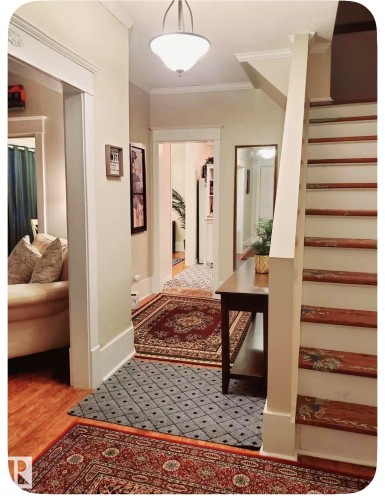 Wood-finish flooring throughout, featuring a staircase with painted risers and wood treads, crown molding, and a hallway with a built-in archway - 10649 125 Street Nw, Edmonton, AB 