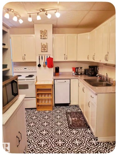 Kitchen featuring white cabinetry, track lighting, a double basin stainless steel sink, a white dishwasher, and patterned floor tile - 10649 125 Street Nw, Edmonton, AB 