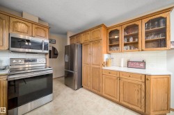 Wood-finish cabinetry with glass-front uppers, stainless steel appliances, white countertops, and tiled backsplash - 