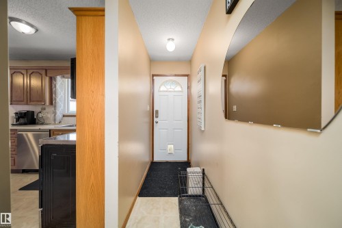 White entry door with decorative glass insert, recessed lighting, and a visible kitchen featuring wood-finish cabinetry and stainless steel appliances - 4104 44 Street, Stony Plain, AB 