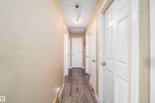 Hallway featuring wood-finish flooring, light neutral wall paint, white trim, and multiple panel doors - 4104 44 Street, Stony Plain, AB 