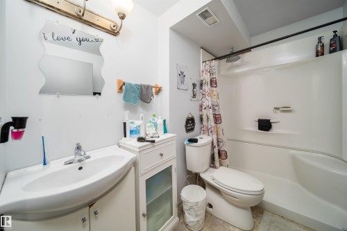 White single-sink vanity with a chrome faucet, light fixture with dual sconces, built-in shelving, and a white tub/shower combination - 4104 44 Street, Stony Plain, AB 