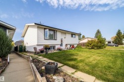 White siding exterior with black trim windows, a concrete pathway, mature landscaping, and a well-maintained lawn - 