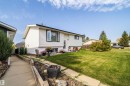 White siding exterior with black trim windows, a concrete pathway, mature landscaping, and a well-maintained lawn - 4104 44 Street, Stony Plain, AB 