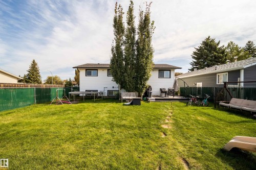 Expansive backyard with a manicured lawn, chain link fencing, a raised deck, and mature trees - 4104 44 Street, Stony Plain, AB 