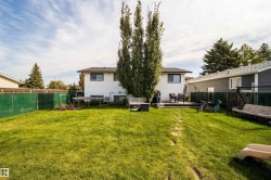 Expansive backyard with a manicured lawn, chain link fencing, a raised deck, and mature trees - 