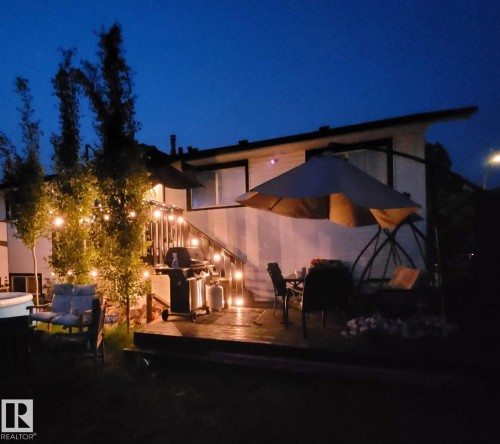 Expansive exterior deck with built-in railing, adjacent to a ground-level patio, featuring string lighting and mature landscaping - 4104 44 Street, Stony Plain, AB 