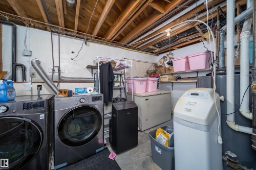 Laundry area featuring a front-loading washing machine and dryer, exposed ceiling joists, and a water treatment system - 4104 44 Street, Stony Plain, AB 