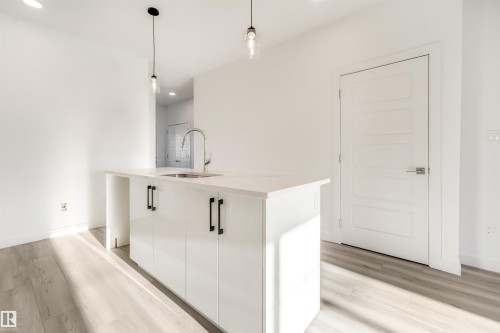 Kitchen island with a built-in sink, stainless steel faucet, and white cabinetry with matte black pulls - 1515 211 Street Nw, Edmonton, AB 