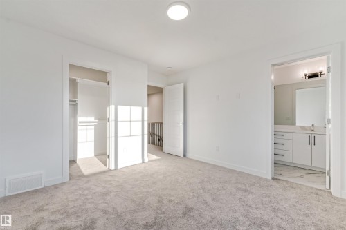 Carpeted room with white walls, an open closet, and a separate bathroom featuring a white vanity with a rectangular sink and a wall-mounted light fixture - 1515 211 Street Nw, Edmonton, AB 