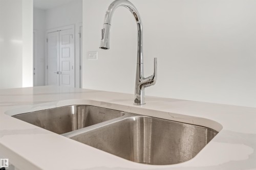 Undermount double basin sink, chrome pull-down faucet, and white countertop with subtle veining - 1515 211 Street Nw, Edmonton, AB 