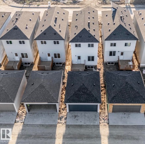 Row of homes featuring light-colored siding, dark shingle roofs, rear decks, and detached garages with concrete driveways - 1515 211 Street Nw, Edmonton, AB 