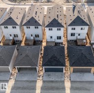 Row of homes featuring light-colored siding, dark shingle roofs, rear decks, and detached garages with concrete driveways - 